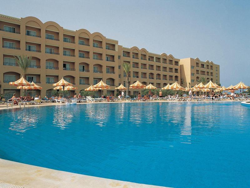 Gran piscina de hotel con sombrillas y tumbonas frente a un edificio hotelero de varios pisos.