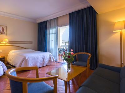 Cozy hotel room with double bed, sofa, armchair, and a table with flowers.