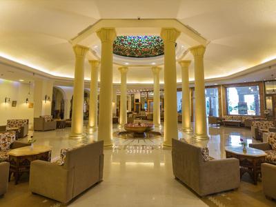 Bright hotel lobby with tall columns, sofas, and a stained glass skylight.