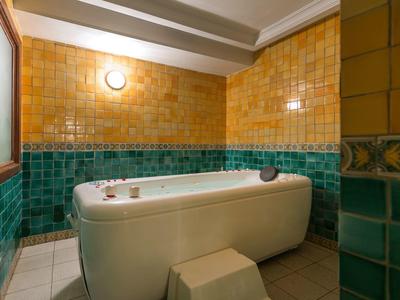 Cozy bathroom with bathtub surrounded by green and yellow tiles under ceiling beams.