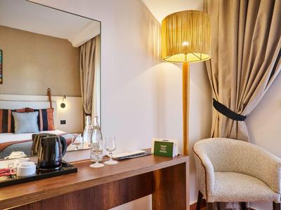 Habitación de hotel con espejo, escritorio, silla y luz de lámpara de pie dorada.
