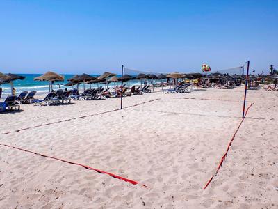 Beach volleyball court on sandy beach with lounge chairs and umbrellas in the background.