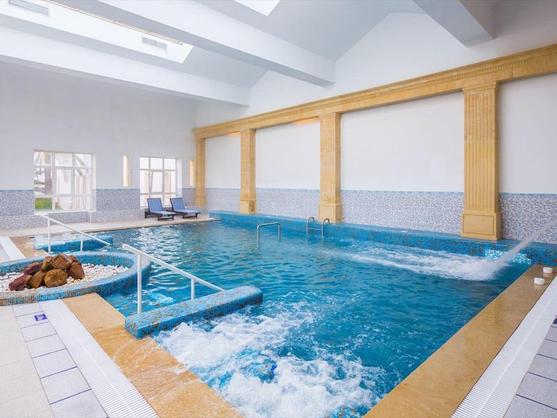 Modern indoor pool with jacuzzi and water loungers in bright room.