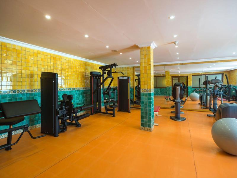 Gym with orange floor, yellow and green tiled walls, and various exercise equipment.