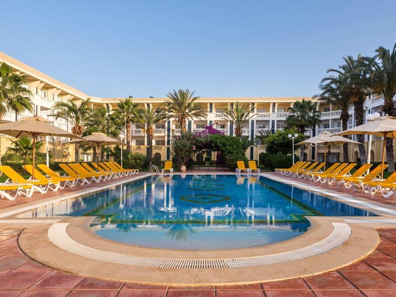 Large pool area with lounge chairs and palm trees at a sunny hotel resort.