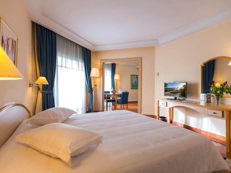 Cozy hotel room with large bed, desk, TV, and warm yellow lighting.