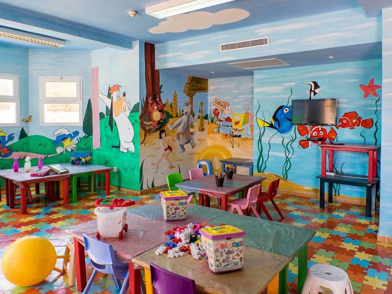 Colorful children's playroom with tables, chairs, and wall murals in a childcare facility.
