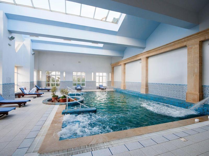 Bright indoor swimming pool with lounge chairs and water features.