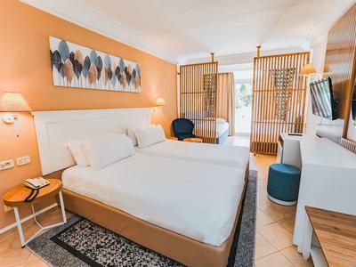 Modernes Hotelzimmer mit großem Bett, Holzmöbeln und warmen orangenen Wänden.