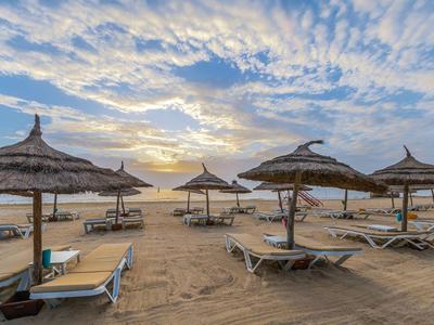 Strand mit Liegestühlen und Strohmundschirmen bei Sonnenaufgang