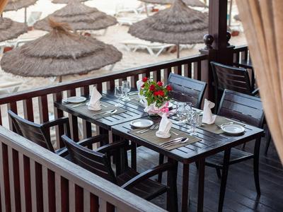 Ein gedeckter Esstisch auf einer Terrasse mit Blick auf einen Strand mit Strohdächern.