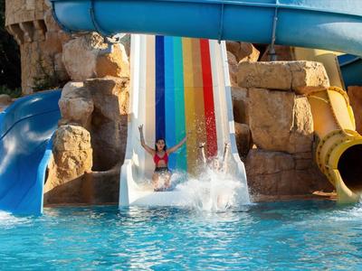 Mehrere bunte Wasserrutschen enden in einem Pool mit Personen, die Spaß haben.