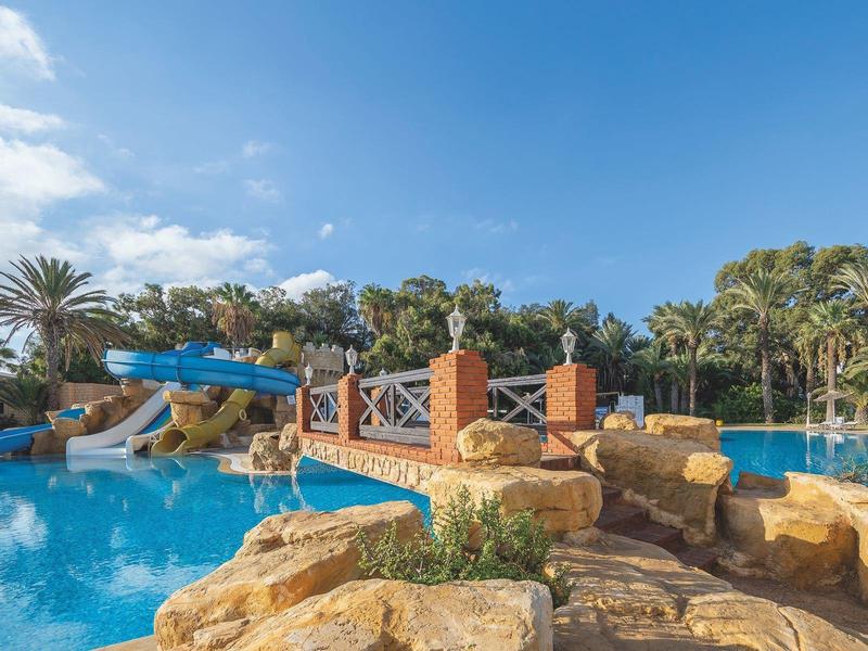Großer Pool mit Wasserrutschen und Palmen in tropischer Ferienanlage.