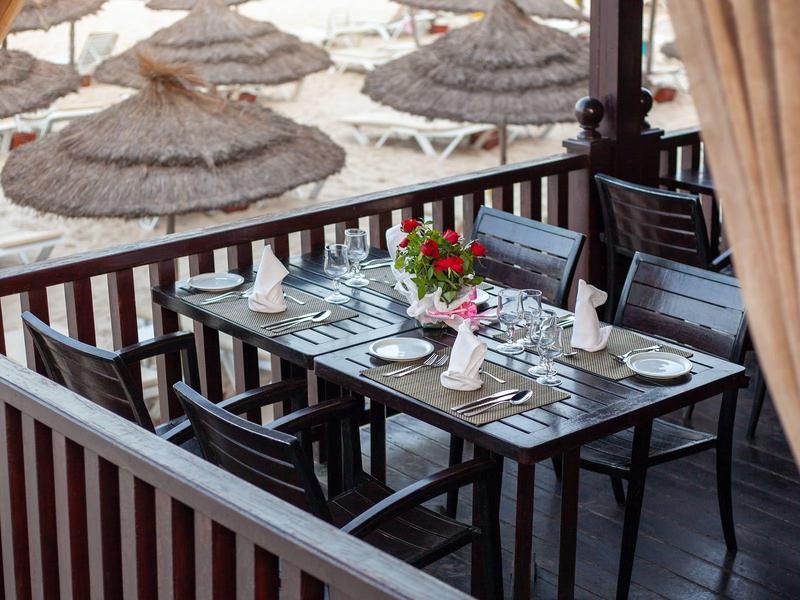 Essbereich auf Balkon mit gedecktem Tisch und Blick auf Strand mit Sonnenschirmen.