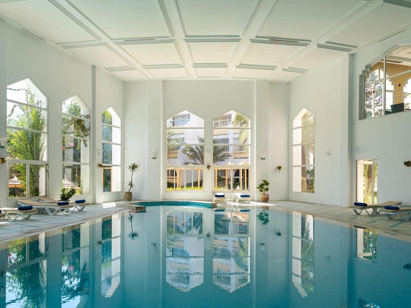 Großes Hallenbad mit weißen Wänden und Sitzbereichen neben dem Wasser