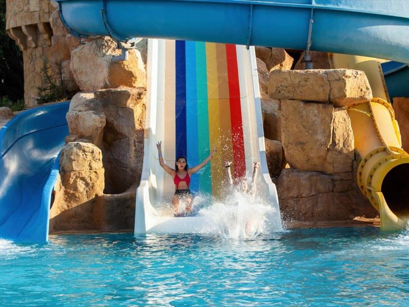 Mehrere bunte Wasserrutschen enden in einem Pool mit Personen, die Spaß haben.