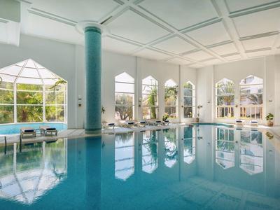 Helles Hallenbad mit großen Fenstern und entspannenden Liegen am Beckenrand.