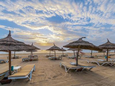 Strand mit Sonnenliegen und Strohmsonnenschirmen bei Sonnenuntergang.