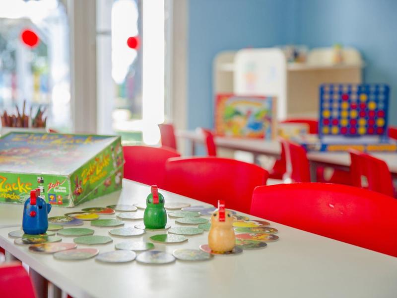 Brettspiele auf einem Tisch in einem farbenfrohen Spielzimmer mit roten Stühlen.