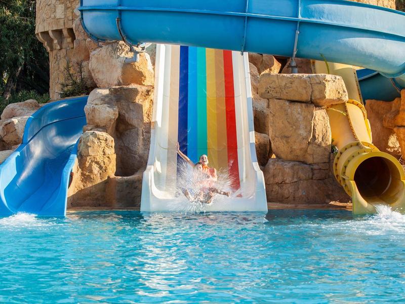 Mehrere Wasserrutschen führen in einen Pool vor Felsenkulisse.
