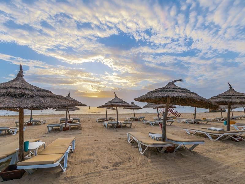 Strand mit Sonnenliegen und Strohmsonnenschirmen bei Sonnenuntergang.