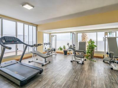 Modernes Fitnessstudio mit Laufband, Trainingsgeräten und großen Fenstern mit Tageslicht.