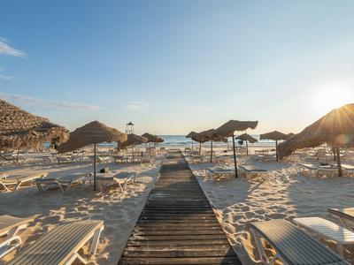 Sonnenuntergang am Strand mit Liegestühlen und Sonnenschirmen entlang eines Holzstegs.