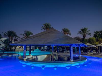 Bar przy basenie z oświetlonym basenem i palmami w tle w nocy