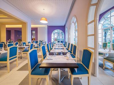 Eleganter Speisesaal mit blauen Stühlen und großen Bogenfenstern, hell und einladend.