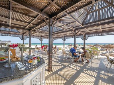 Offener Essbereich mit Tischen, Stühlen und Blick aufs Meer unter Holzpergola