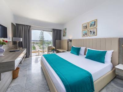 Nowoczesny pokój hotelowy z dużym łóżkiem, turkusowymi akcentami i balkonem z widokiem.