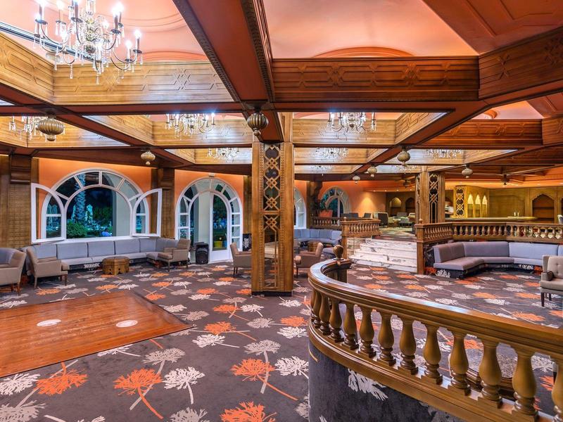 Elegancki hotelowy salon z drewnianymi sufitami, kolorowym dywanem i wygodnymi miejscami do siedzenia.