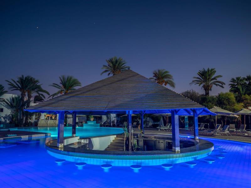 Bar przy basenie z oświetlonym basenem i palmami w tle w nocy