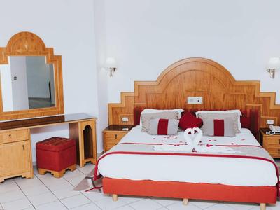 Hell eingerichtetes Hotelzimmer mit großem Bett, Nachttischen und Schminktisch mit Spiegel.