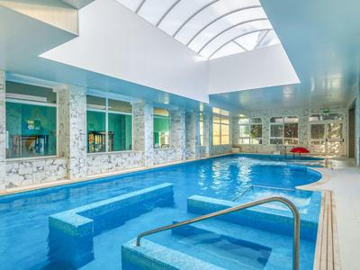 Helles Schwimmbad mit rechteckigem Becken, Glasdach, Steinwänden und blauen Fliesen.