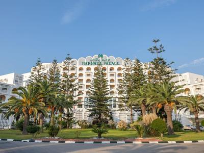 Großes, weißes Hotel mit vielen Balkonen, umgeben von Palmen und blauem Himmel im Hintergrund.