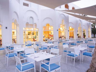 Freiluftrestaurant mit weißen Tischen und blauen Stühlen vor hell erleuchteten Bögen.