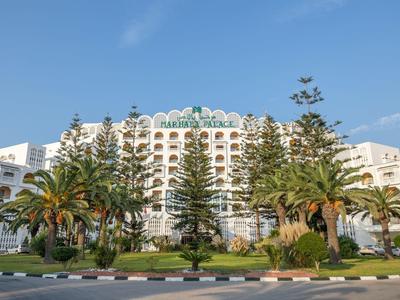 Grande hotel bianco con palme e cielo blu parzialmente nuvoloso sullo sfondo.