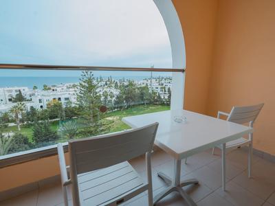 Balcone con tavolo bianco e due sedie con vista sul giardino e sul mare.