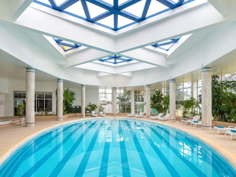 Piscina interna moderna con luce naturale e colonne bianche in un hotel.