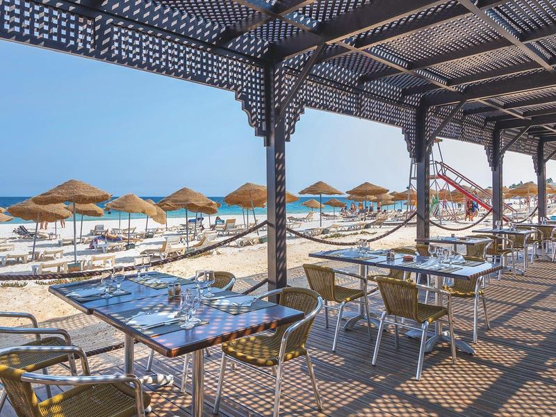 Terrazza di un ristorante sul mare con vista sulla spiaggia e ombrelloni di paglia.