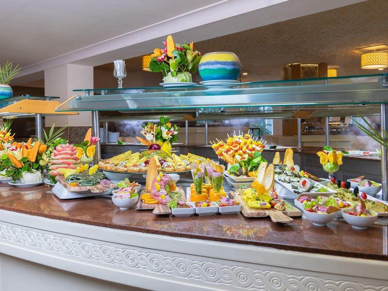 Buffet vario con frutta, verdura, formaggi e dolci in un ambiente moderno di hotel.