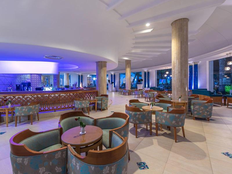 Lounge d'hotel moderno con poltrone, tavoli rotondi e illuminazione ambientale blu.