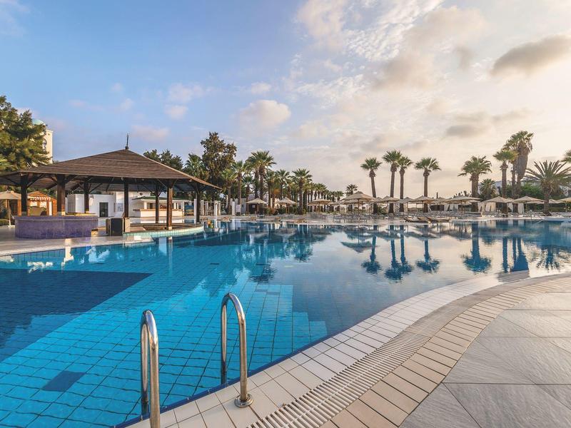 Piscina di hotel con palme e cielo parzialmente nuvoloso al tramonto.