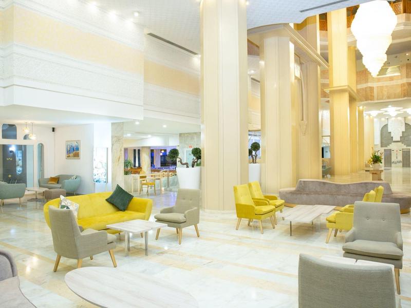 Luminoso atrio di hotel con colonne bianche, sedute moderne e luce calda.