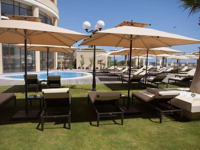 Taras hotelowy z leżakami, parasolami i basenem pod czystym niebem.