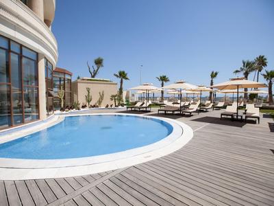 Basen kryty z drewnianym tarasem, leżakami i parasolami pod czystym błękitnym niebem.