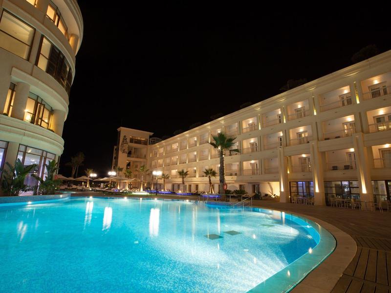 Oświetlony hotelowy basen z wielopiętrowym budynkiem w nocy.