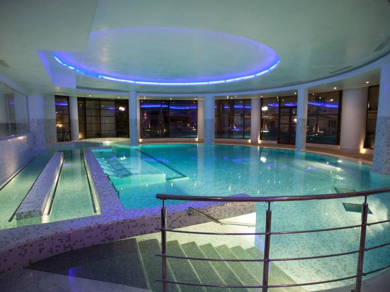 Nowoczesny, oświetlony kryty basen hotelowy z oknami ze szkła i schodami.