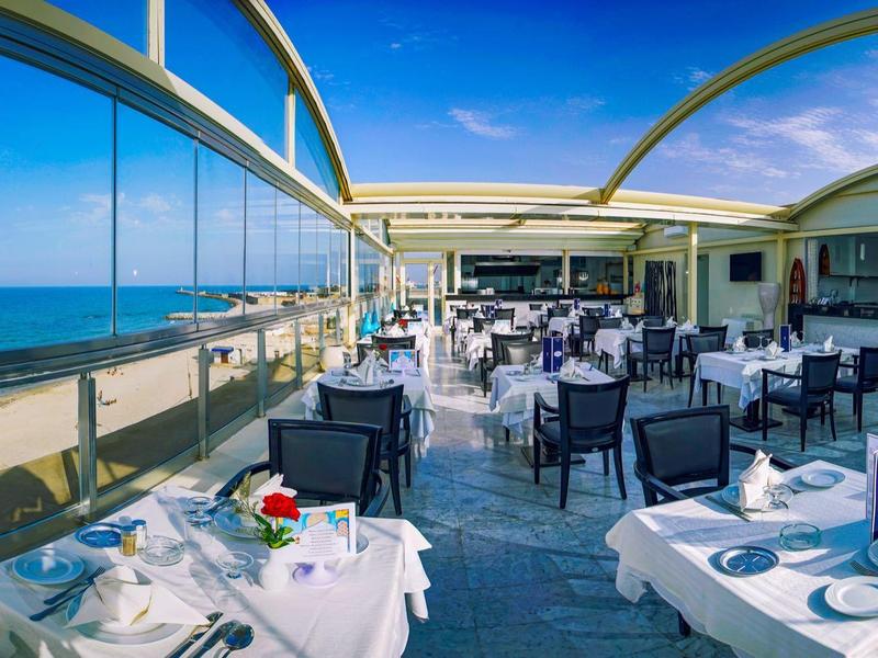 Otwarta restauracja z białymi obrusami i widokiem na morze pod błękitnym niebem.